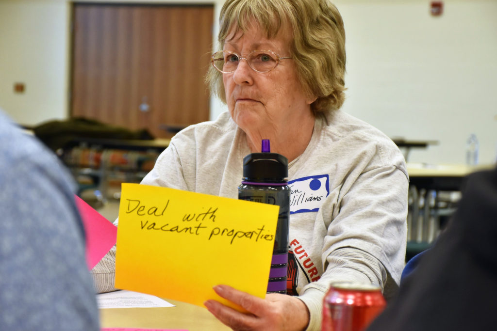 A woman holds up a large sticky note that reads "Deal with Vacant Properties"