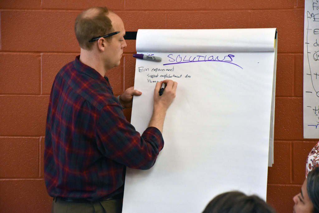 A man writes on a large white notepad that says "solutions". 