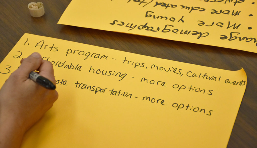 A hand writing on a large sticky note what they would improve about their community.