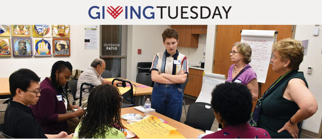 A group of people gathered around a table with Giving Tuesday written about the photo.