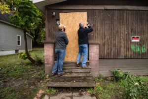 Summit-County-Land-Bank-program-director-Jim-Davis-and-staff-attorney-Drew-Reilly-secure-a-plywood-over-the-front-door-at-426-McGowan-St.-H.L.-Comeriato